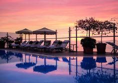 an empty pool with lounge chairs and umbrellas in front of the water at sunset