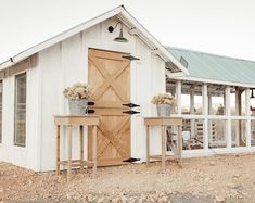 a small white shed with two planters on the outside and a table in front