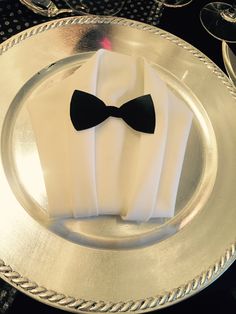 a silver plate topped with a black bow tie and white napkins on top of it