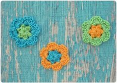 three crocheted flowers sitting on top of a blue wooden table next to each other