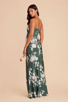 a woman wearing a green floral print dress with spaghetti straps and open back, standing in front of a beige background