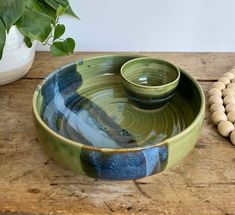 two bowls sitting on top of a wooden table next to a bead necklace and potted plant