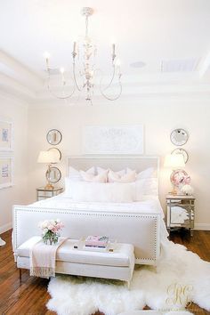 a bedroom with a white bed and chandelier in the corner, on top of a hard wood floor