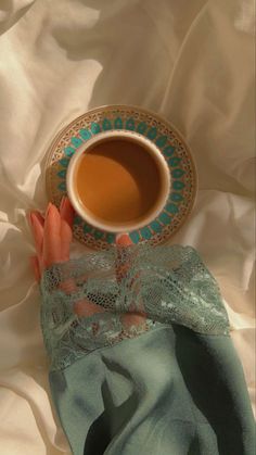 a woman's hand holding a cup of tea on top of a white sheet