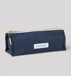 a blue canvas pouch with a white label on the front and gold zippered closure