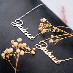 three personalized name necklaces sitting on top of a black leather surface with dried flowers