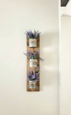 three mason jars filled with lavender flowers on a wooden wall hanging from a white wall