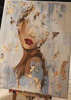 a painting on an easel with gold paint splattered all over it and a woman's face