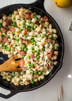 a skillet filled with macaroni and peas on top of a white table