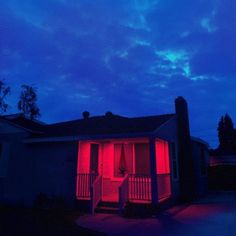 a house is lit up with red light in the front yard and on the porch