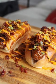 two hot dogs covered in chili and cheese sitting on a cutting board next to each other