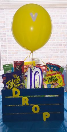 a box filled with snacks and balloons on top of a blue tablecloth covered table