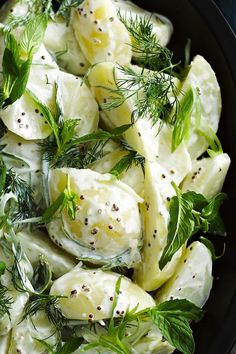 a black bowl filled with cucumber and dill garnished with herbs