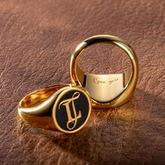 two gold wedding rings with the word love you written on them, sitting next to each other