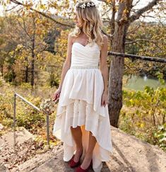 a woman wearing a white dress and red shoes standing on the edge of a cliff