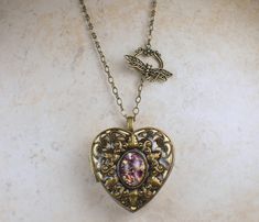 Music box pendant. This heart shaped music box pendant is inspired by the gorgeous music box pendants of era's gone by. Music box is pill box size, please look at the dimensions for exact size. A perfect bronze heart locket has been adorned with a layer of filigree and a amethyst glass fire opal cabochon. The cabochon is set in a bronze bezel. The filigree and bronze bezel have been finished with resin to preserve the beauty of this pendant. The music box winds from a key on the back of the pend Purple Locket, Collectible Heart-shaped Locket Jewelry, Music Box Locket Necklaces, Music Box With Key Necklace, Music Box Pendant, Photo Locket, Necklace Box, Heart Locket, Funky Jewelry