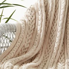 a white blanket sitting on top of a chair next to a plant