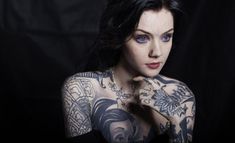 a woman with tattoos on her arms and chest posing for a photo in front of a black background