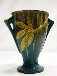 a green vase with yellow flowers painted on it's sides and the bottom part of its body