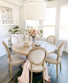 a dining room table with white chairs and flowers