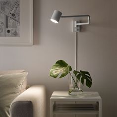 a white table with a green plant on it next to a couch and framed pictures