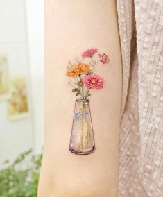 a woman's arm with flowers in a vase tattoo on the left inner arm