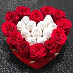 a heart shaped box filled with white and red roses on top of a black table