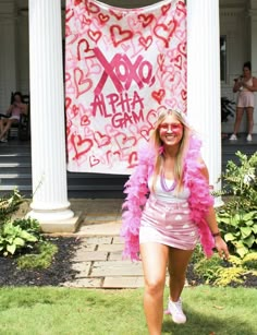 a woman walking in front of a building with a pink banner behind her and hearts on the wall