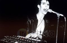 a man with headphones on singing into a microphone while holding a keyboard in front of him