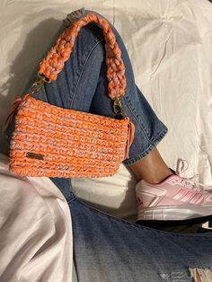 an orange purse sitting on top of a bed next to a pair of jeans and sneakers