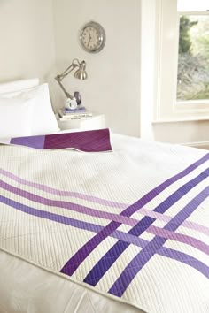 a bed with a purple and white quilt on top of it next to a window