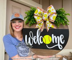 a woman holding up a welcome sign with a softball ball on it and a bow