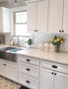 a kitchen with white cabinets and marble counter tops is pictured in this image, there are vases on the window sill