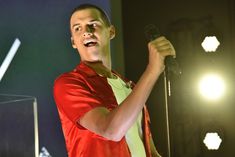 a man standing in front of a microphone on stage with his hand up to the air