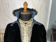 Black velvet coat, ca. 1915, provenance: America, Valentine Museum. Label is no longer decipherable. Collar and cuffs are made of blue moiré silk and decorated with rabbit fur. Appliquéd cord decoration on the back. Wide belt that fastens with press studs; decorated with ball studs (one button missing). In the lower third, the velvet is replaced by a black silk ottoman pendant skirt. A blue ribbon also marks the transition. The inside is lined with blue silk (only in the area of the velvet; the Victorian Costume Outerwear For Fall, Victorian Style Costume Outerwear For Fall, Victorian Fall Costume Outerwear, Victorian Outerwear With Historical Design For Costume, Victorian Historical Outerwear For Costumes, Victorian Style Historical Costume Outerwear, Vintage Outerwear With Historical Design For Costume, Vintage Costume Outerwear With Historical Design, Regency Style Long Sleeve Costume Outerwear