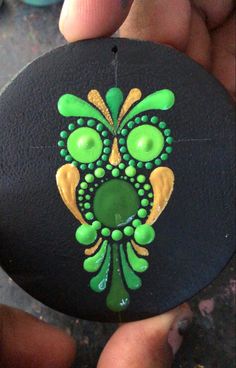 a hand holding a black rock with green and yellow designs on it's face