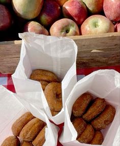 there are three bags of donuts on the table with apples in the back ground