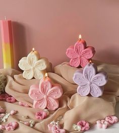 some pink and purple candles are on a table next to other flowers, with a candle in the background