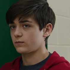 a close up of a person wearing a red hoodie and looking at the camera