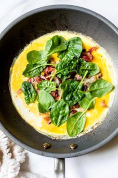 an omelet with spinach and bacon in a pan on a white table