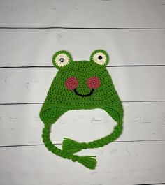 a crocheted frog hat with eyes and ears on top of a white wall