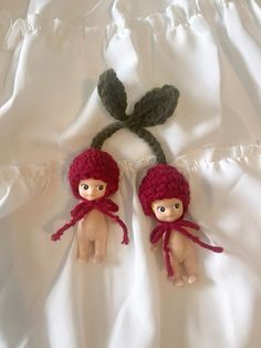 two little dolls are laying on a white sheet with one doll wearing a red knitted hat