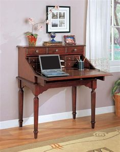 a laptop computer sitting on top of a wooden desk in front of a window with curtains