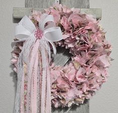 a pink and white wreath hanging on the side of a wooden wall next to a cross