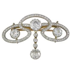 An Art Nouveau diamond scroll brooch, the brooch comprising three old brilliant-cut diamonds, within a flowing openwork diamond-set scroll surround, with old brilliant-cut diamond drop to the centre, the diamonds estimated to weigh a total of 3.2 carats, all set in platinum with grain edging to a yellow gold mount and brooch fitting, English, circa 1900, measuring approximately 3.8x2.5cm, gross weight 7.1 grams, illustrated in "Jewelry For Gentlemen" by James Sherwood, pages 144 & 145. A dazzling Edwardian brooch. This brooch features a sinuous openwork design set with glittering diamonds. The three old cut diamonds to the centre of the frame scintillate beautifully and are surrounded by further lively diamonds set into the scroll surround. This lovely and sparkling brooch comes from the c Edwardian Jewelry, Antique Brooches, Sterling Silver Brooch, Diamond Brooch, Gold Brooches, Bespoke Jewellery, Silver Brooch, Lovely Jewellery, Selling Jewelry