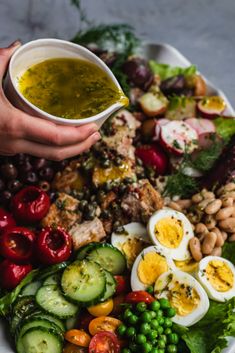 someone is pouring dressing into a salad with hard boiled eggs, cucumbers, tomatoes, peas and other vegetables