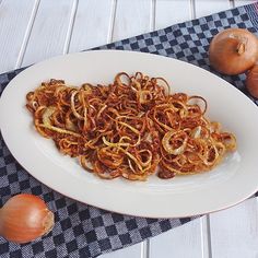 a white plate topped with noodles next to onions and an onion on a checkered table cloth