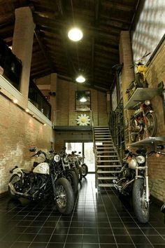 two motorcycles are parked next to each other in a room with stairs leading up to the second floor