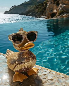 a gold duck wearing sunglasses sitting on the edge of a swimming pool