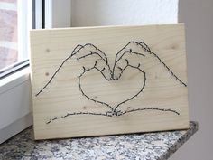 two hands making a heart with their fingers on a piece of wood next to a window